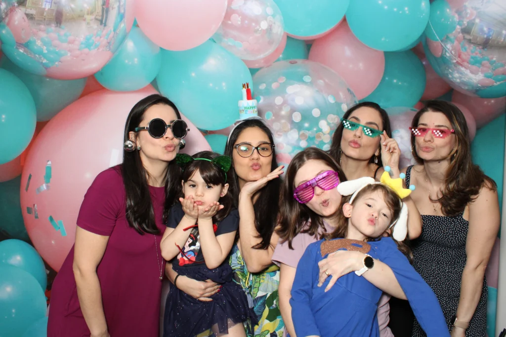 Moms, kids and friends of every age in party glasses together at a Prismatic open-air photo booth with a balloon wall