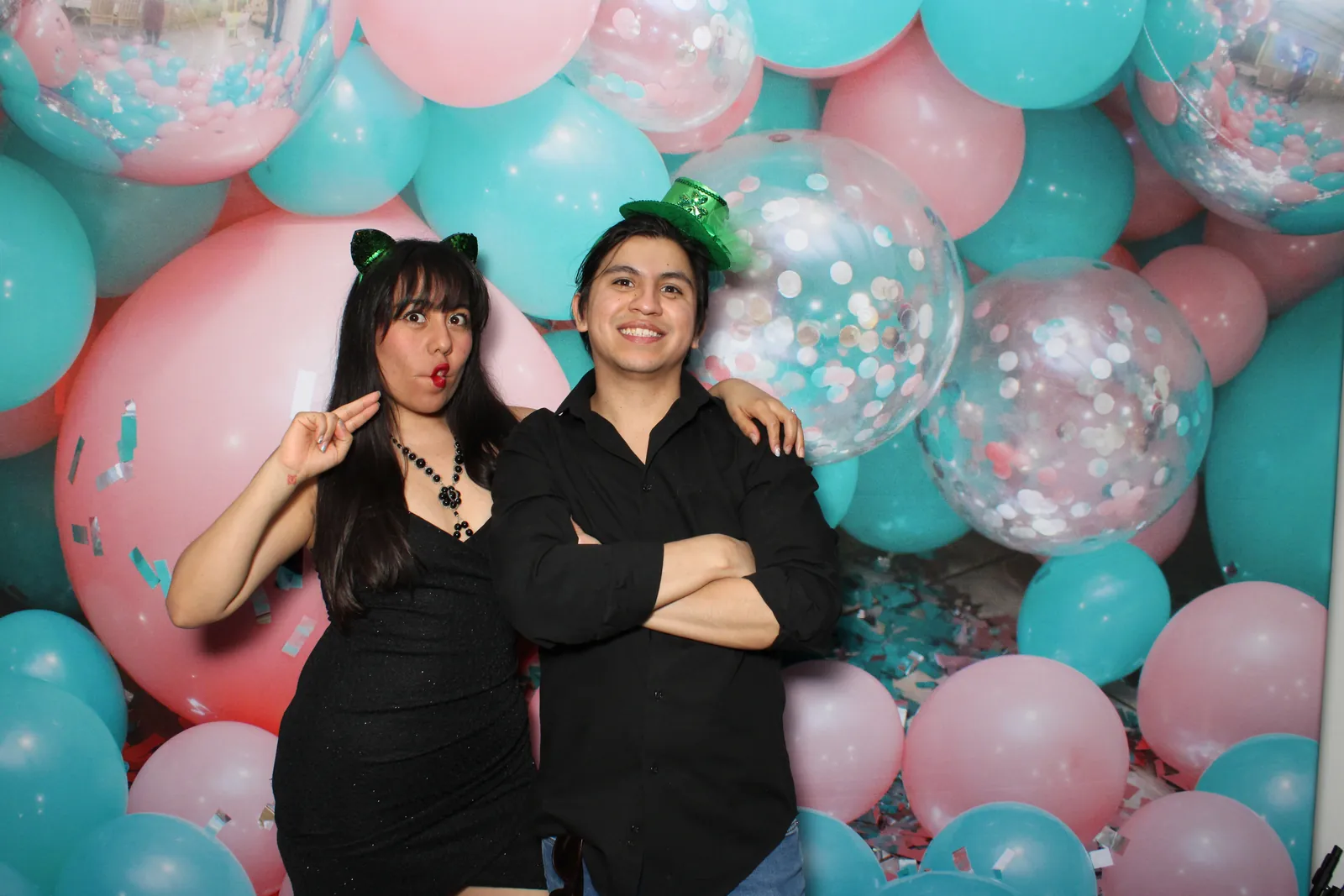 Two guests posing in front of a pink and teal balloon wall
