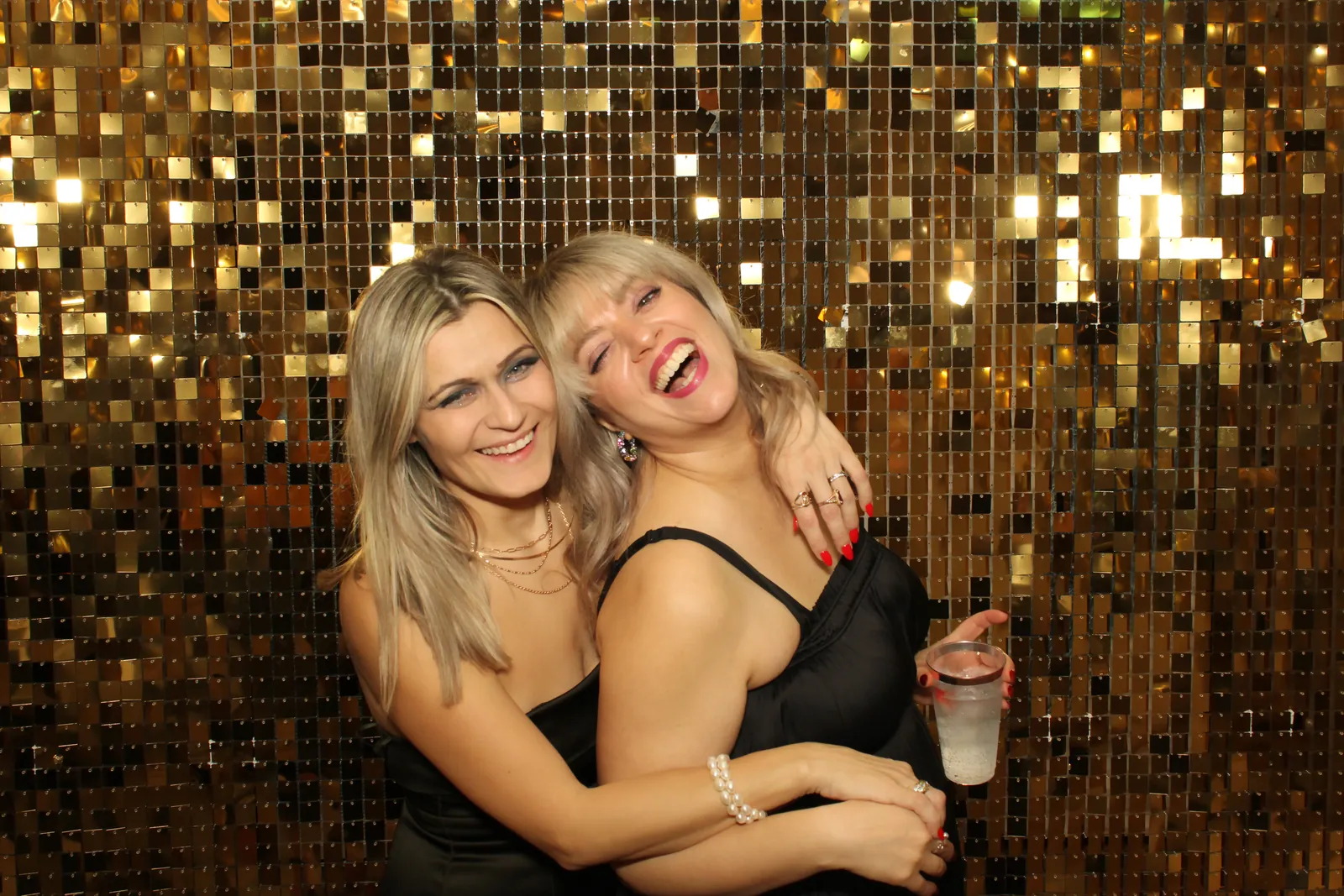 Two friends laughing at a gold sequin photo booth