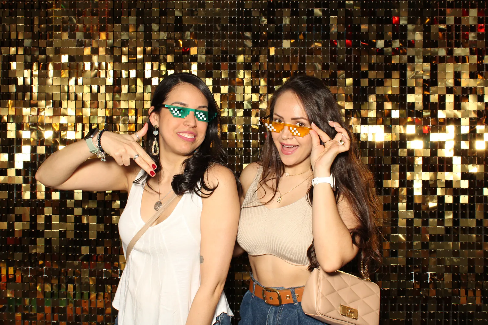 Two friends in party sunglasses at a gold sequin photo booth