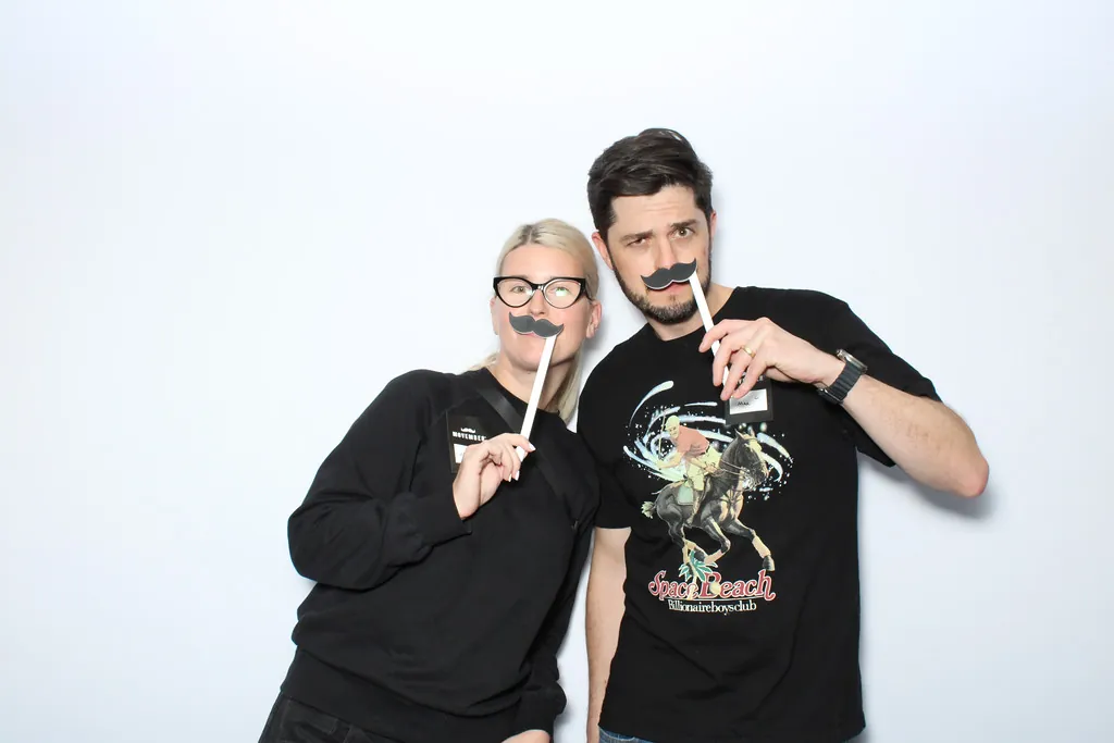 Two guests with mustache props on a clean white backdrop